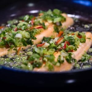 Asian-Style Marinade Trout fillets sizzling in a pan with fresh vegetables