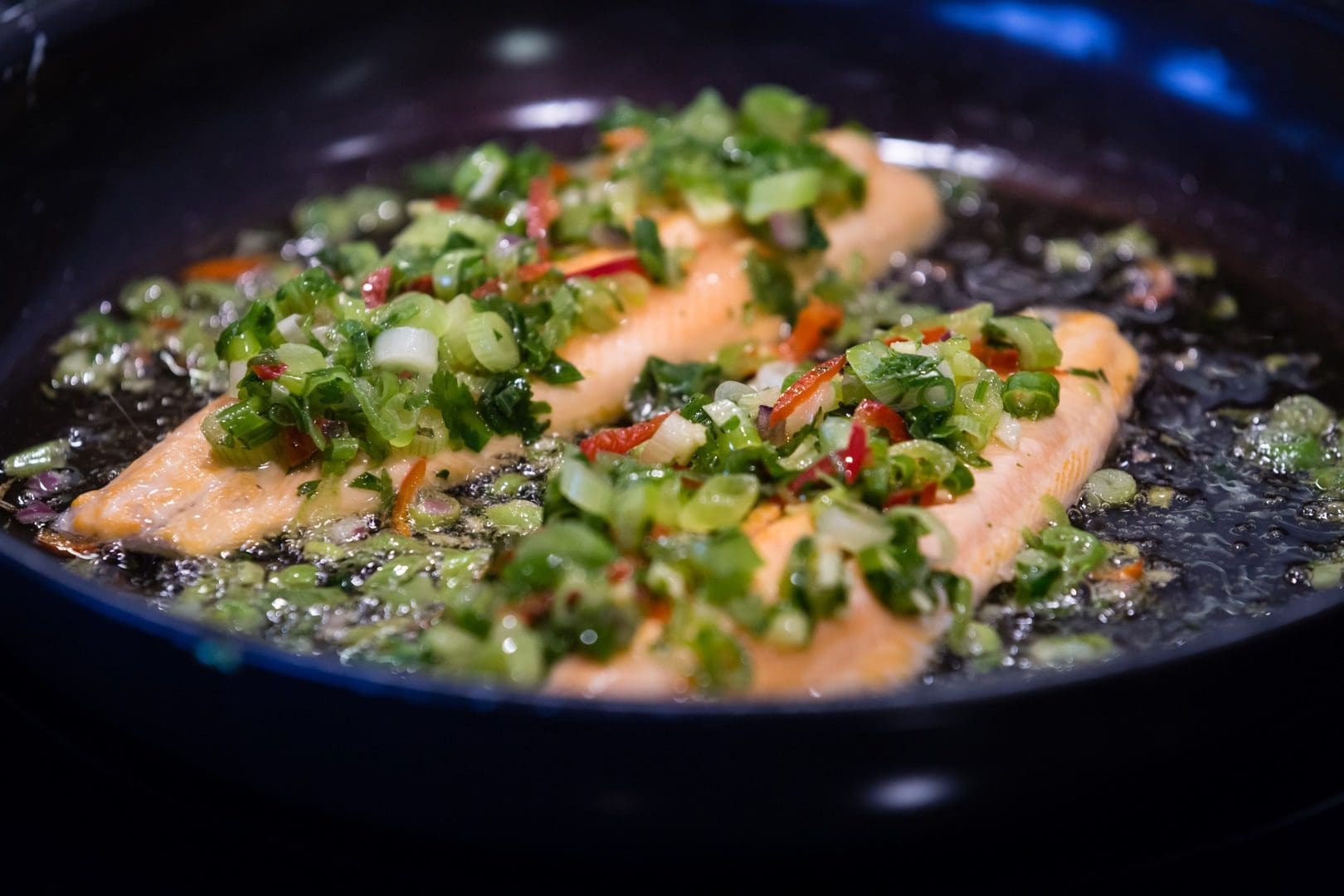Asian-Style Marinade Trout fillets sizzling in a pan with fresh vegetables