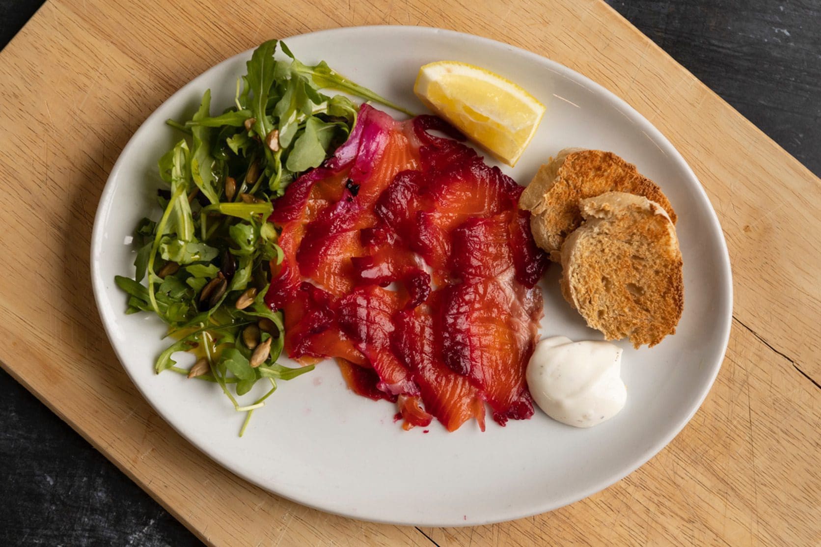 beetroot and gin gravalax Close-up of slices of beetroot-cured trout arranged on a bed of fresh salad greens, served with slices of crusty bread.