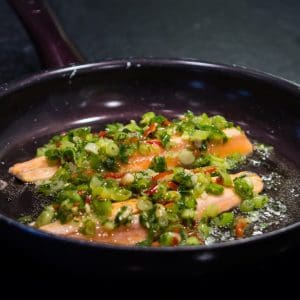 Trout fillet sizzling in a black frying pan.